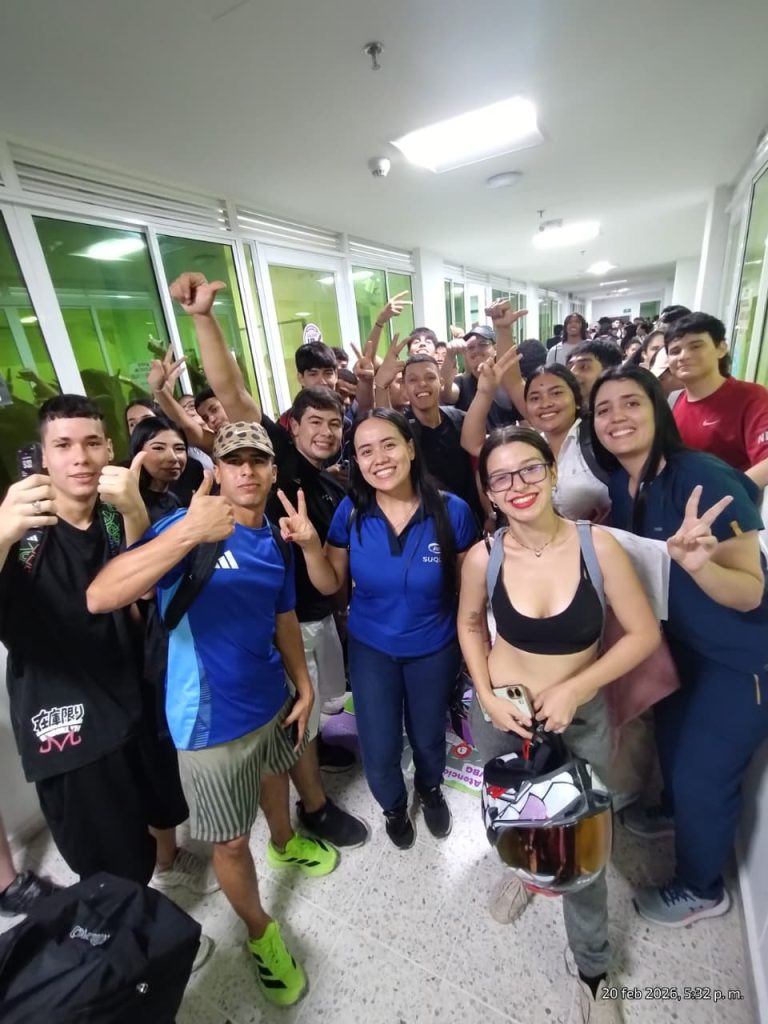 Grupo numeroso de estudiantes posando con una profesional de Bienestar Institucional en un pasillo del campus.