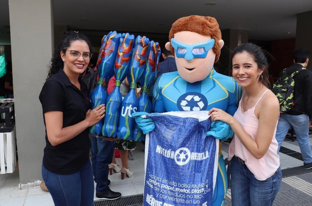 Dos estudiantes y la mascota institucional sostienen una bolsa reutilizable en una jornada ambiental.