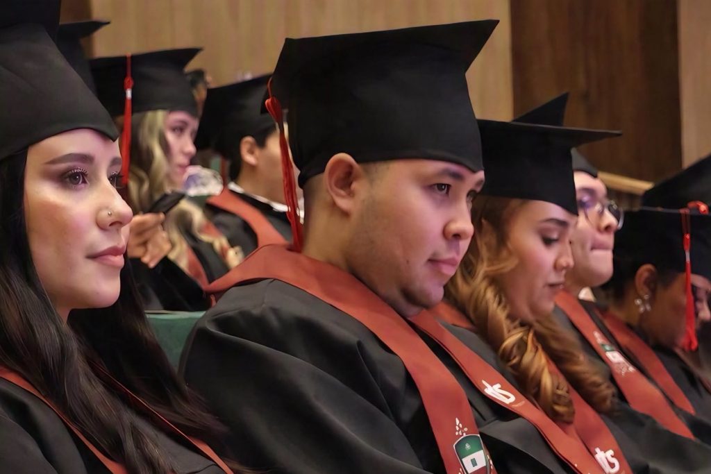 Graduandos de la UTS sentados en el auditorio durante la ceremonia, con toga negra, birrete y estola.