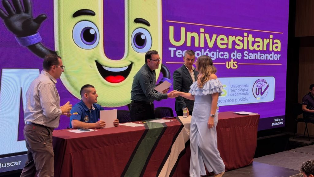 Una asistente recibe su certificado en el escenario, frente a la mascota de la UTS