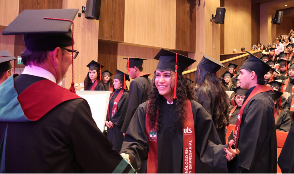 Una graduada con toga y birrete recibe el saludo de un directivo durante la ceremonia de grado.