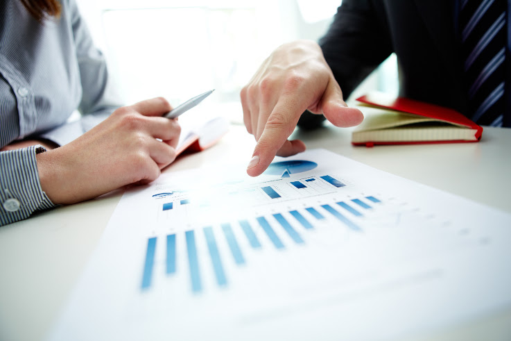 Dos personas revisan sobre una mesa un informe con gráficas de barras