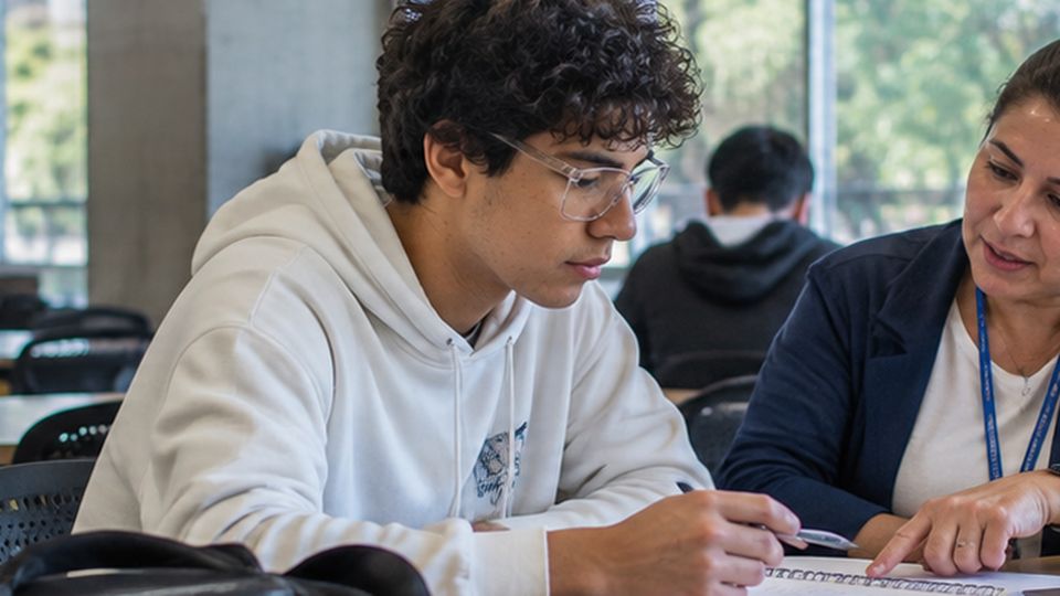 Un estudiante y una asesora revisan unos documentos en una mesa de trabajo.